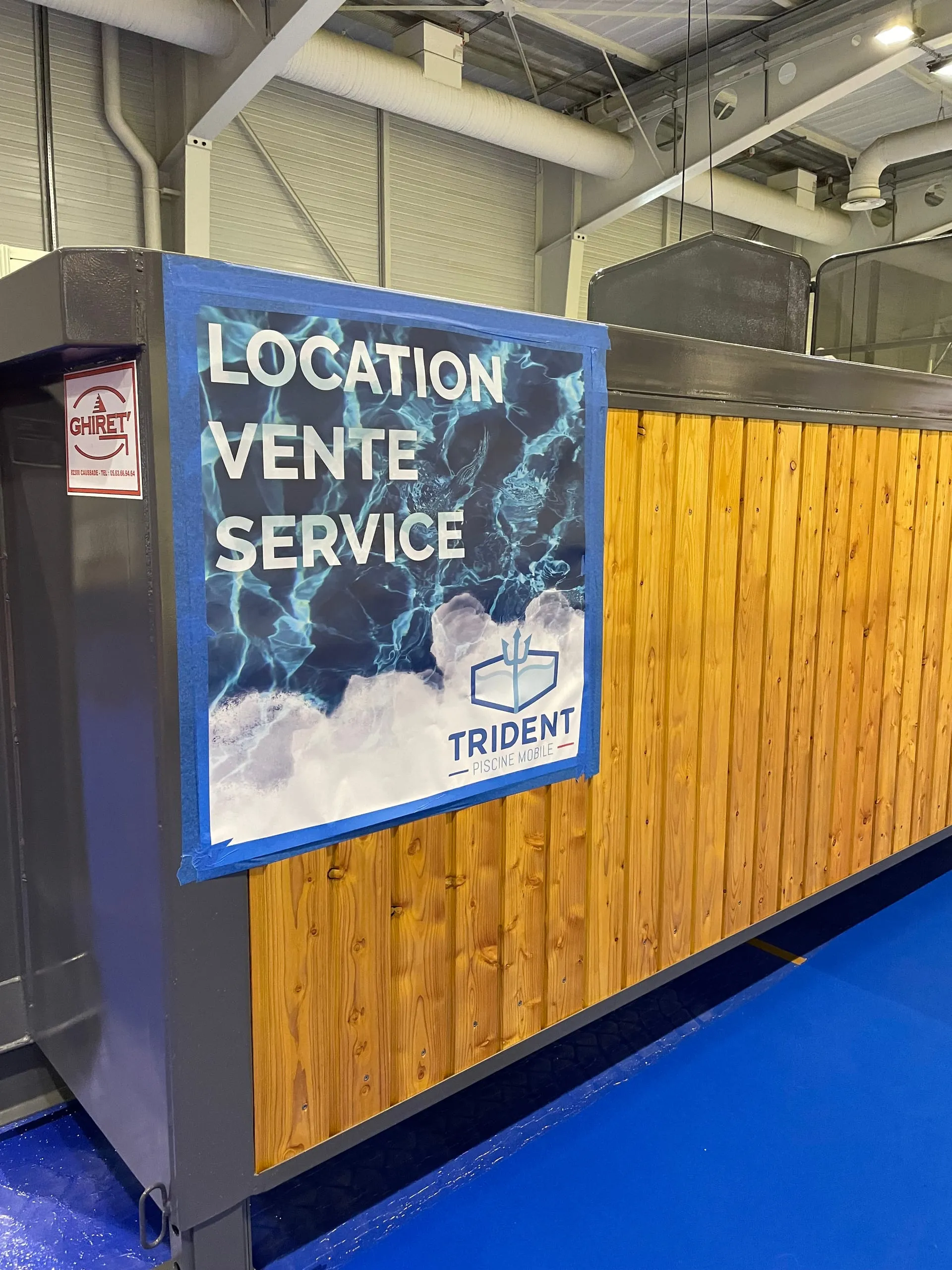 Flanc d’une piscine container mobile Trident Piscine en exposition, affiche Location Vente Service et habillage bois.