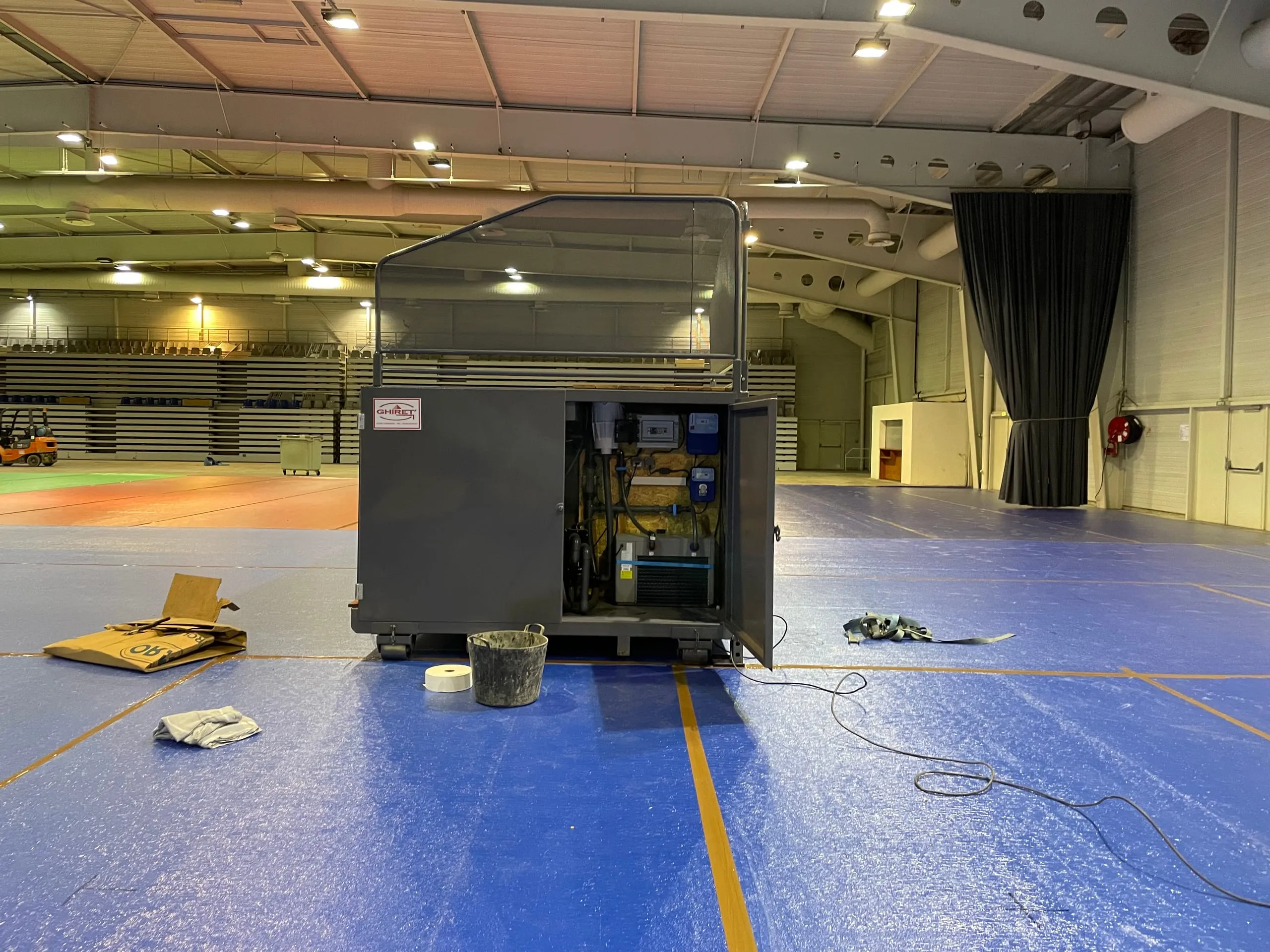 Bloc de filtration ouvert d'une piscine container mobile Trident Piscine lors d'une installation dans un gymnase, pompes et tableau de commande visibles.