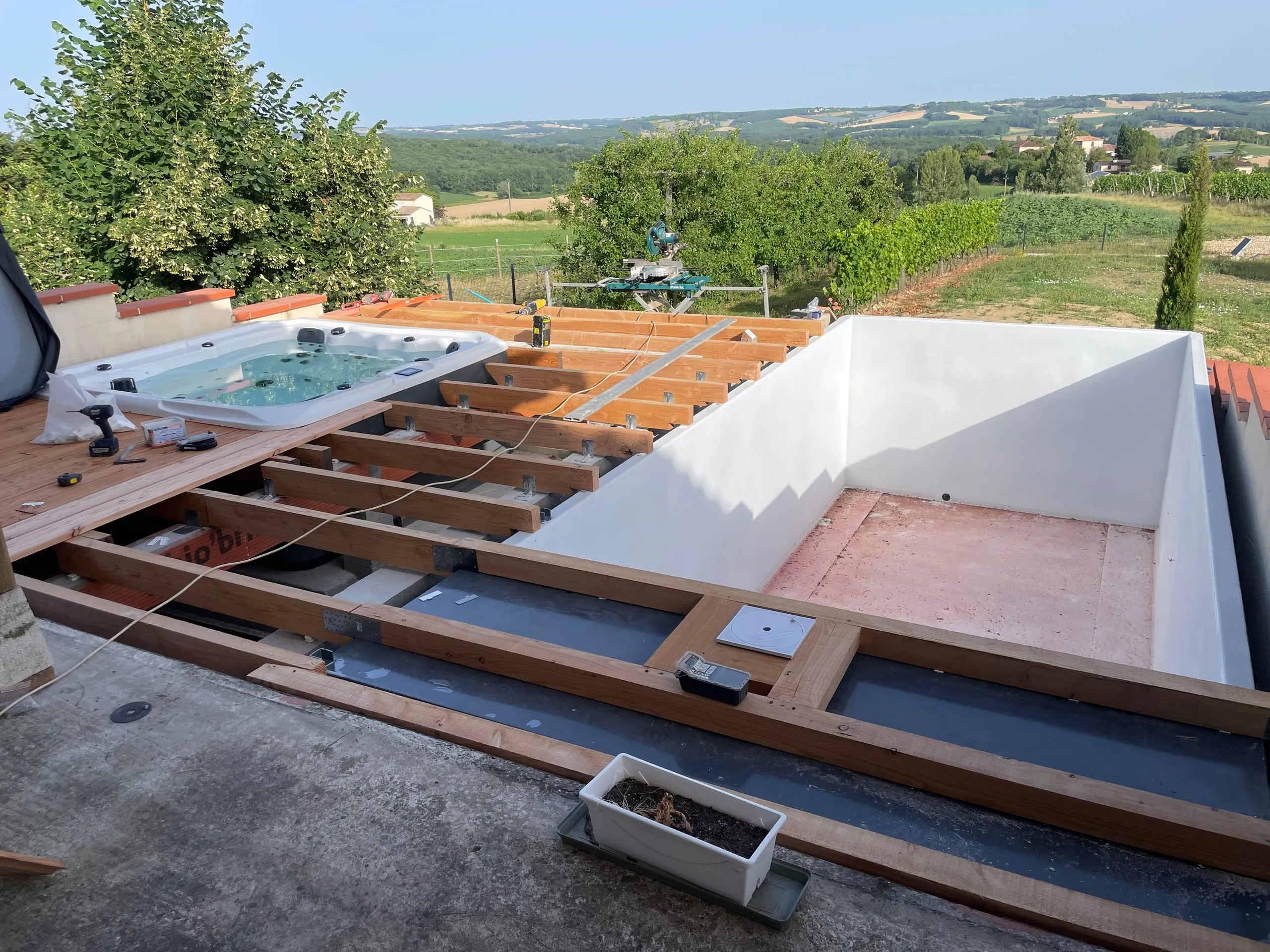 Chantier d'installation d'une piscine mobile avec pose de terrasse bois, vue panoramique sur la campagne
